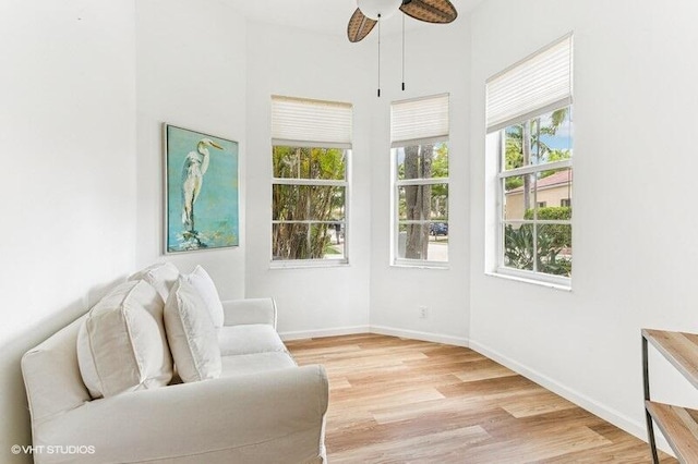 living area with light wood-style floors, baseboards, ceiling fan, and a towering ceiling