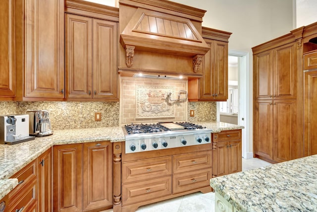 kitchen featuring brown cabinets, light stone counters, backsplash, stainless steel gas cooktop, and custom range hood