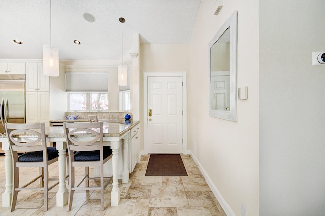 kitchen with white cabinets, a peninsula, baseboards, built in fridge, and a breakfast bar area