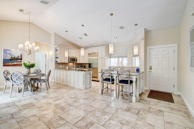 kitchen featuring lofted ceiling, decorative backsplash, an inviting chandelier, a peninsula, and appliances with stainless steel finishes