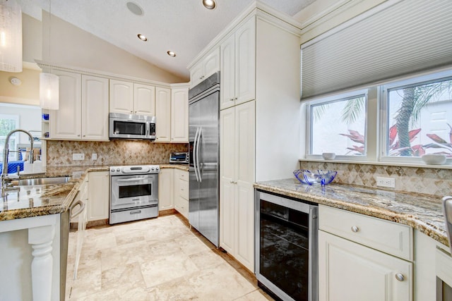 kitchen with a sink, vaulted ceiling, light stone counters, beverage cooler, and appliances with stainless steel finishes