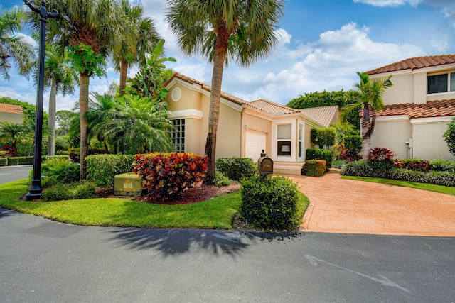 mediterranean / spanish house featuring stucco siding, a tiled roof, decorative driveway, and a garage