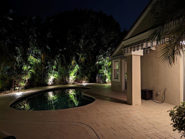 pool at night featuring an outdoor pool and a patio