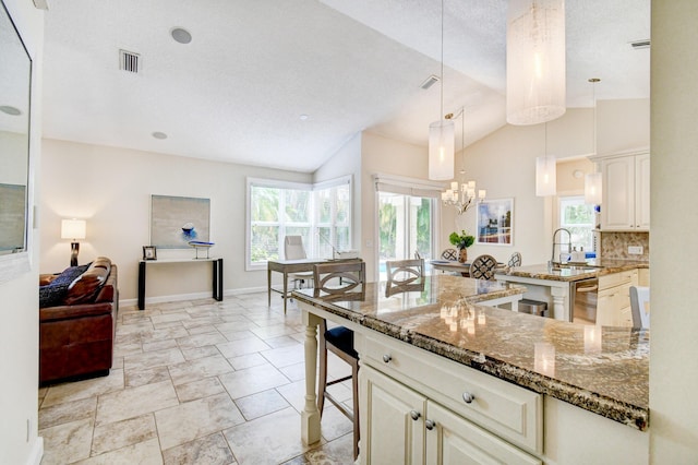 kitchen with a sink, dark stone countertops, vaulted ceiling, a kitchen bar, and dishwasher