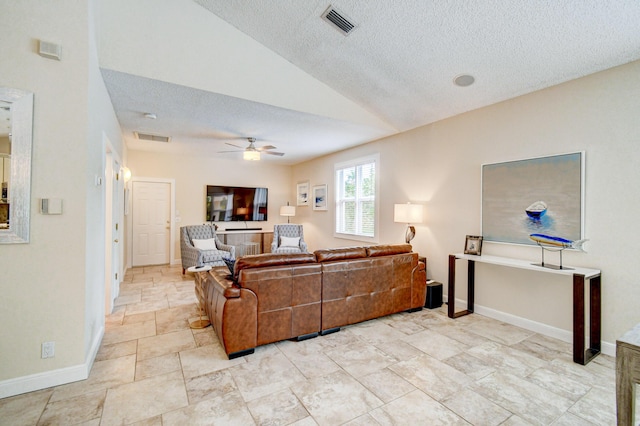 living area with a textured ceiling, vaulted ceiling, baseboards, stone finish floor, and ceiling fan