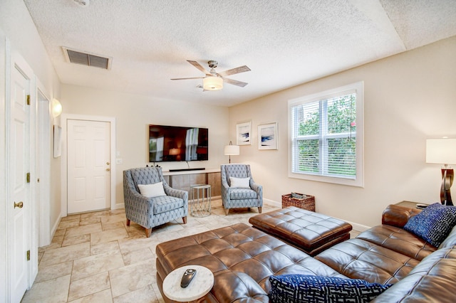 living area with baseboards, a ceiling fan, visible vents, and a textured ceiling