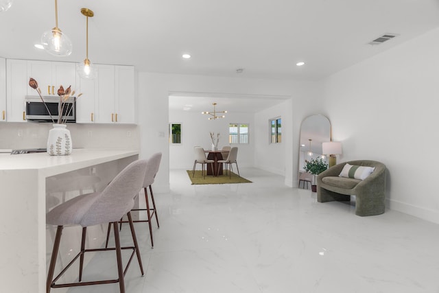 2771 NE 53rd St, Lighthouse Point, FL 33064 - kitchen featuring a kitchen breakfast bar, stainless steel microwave, white cabinetry, marble finish floor, and decorative light fixtures