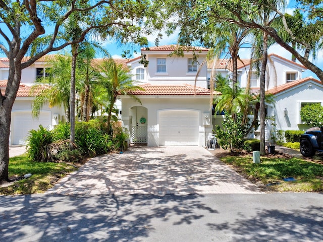 mediterranean / spanish-style home with stucco siding, an attached garage, a tiled roof, and decorative driveway
