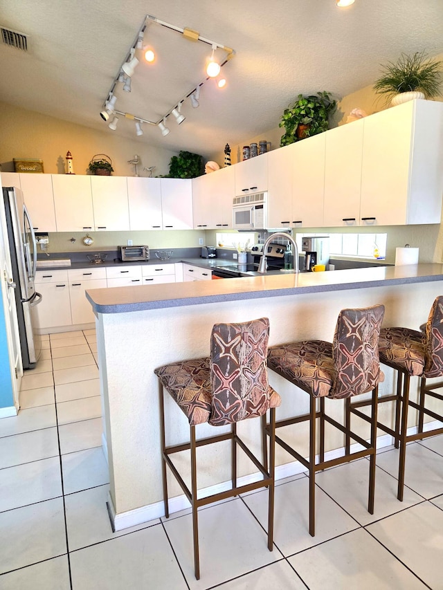 kitchen featuring light tile patterned floors, track lighting, a breakfast bar area, stainless steel appliances, and visible vents