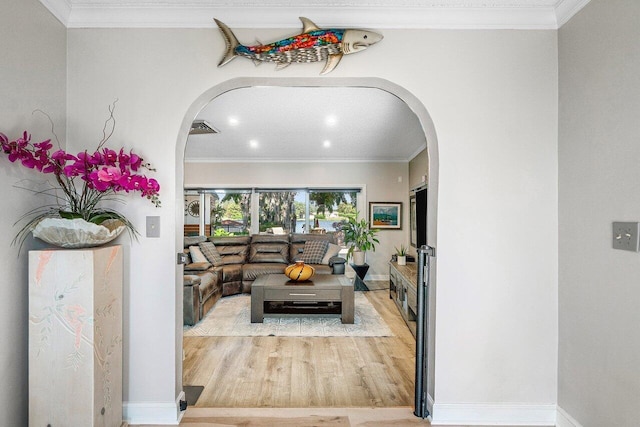 living area with crown molding, wood finished floors, arched walkways, baseboards, and visible vents