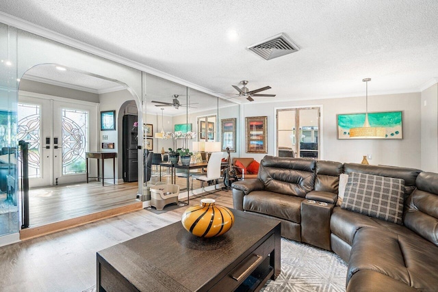 living area featuring visible vents, arched walkways, light wood-style flooring, a textured ceiling, and ceiling fan