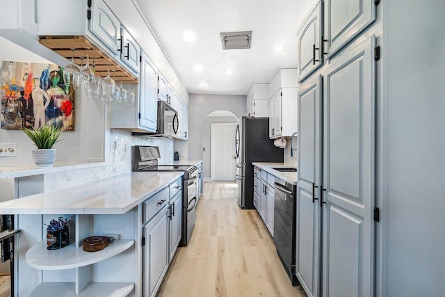 kitchen with stainless steel appliances, open shelves, arched walkways, light wood-style floors, and decorative backsplash