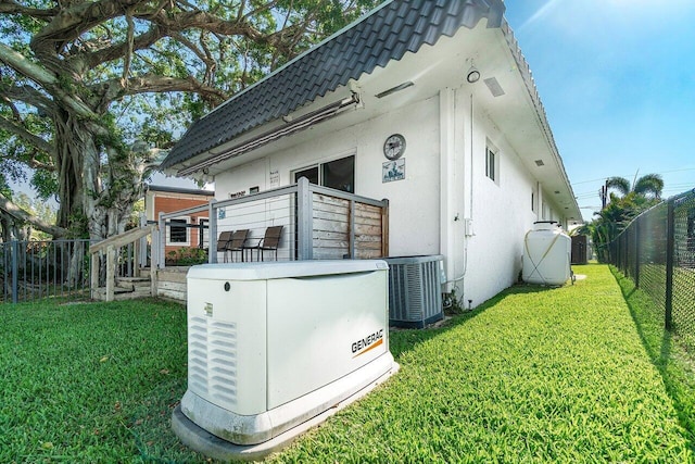 back of property featuring stucco siding, central AC unit, fence, and a yard