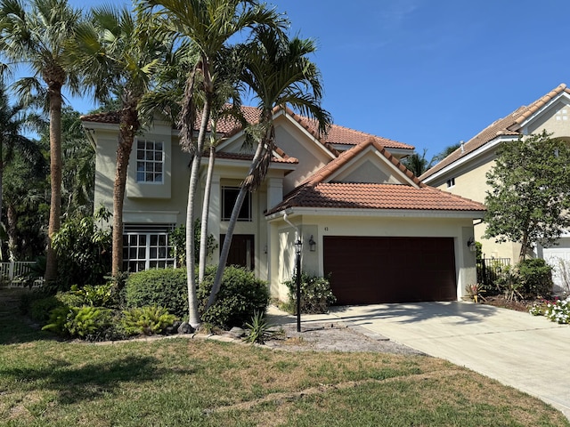 mediterranean / spanish home featuring stucco siding, an attached garage, concrete driveway, a tiled roof, and a front yard