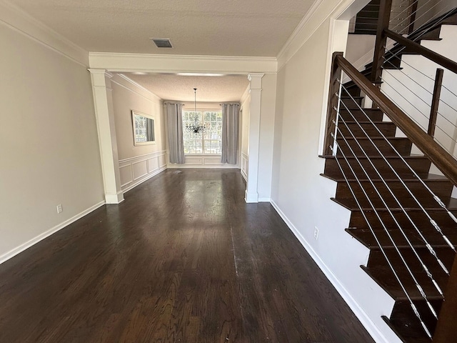 hallway featuring wood finished floors, crown molding, decorative columns, stairs, and a chandelier