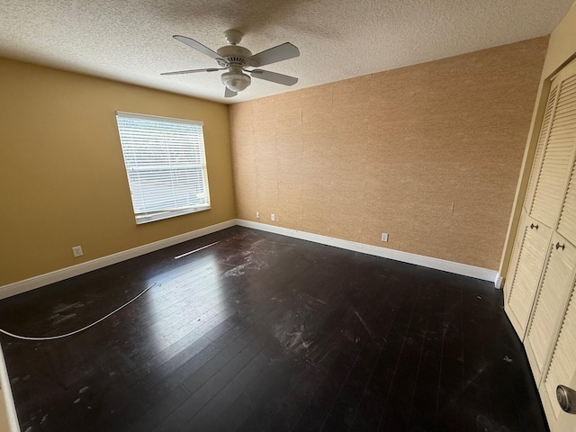 unfurnished bedroom featuring dark wood-type flooring, a closet, baseboards, a textured ceiling, and ceiling fan