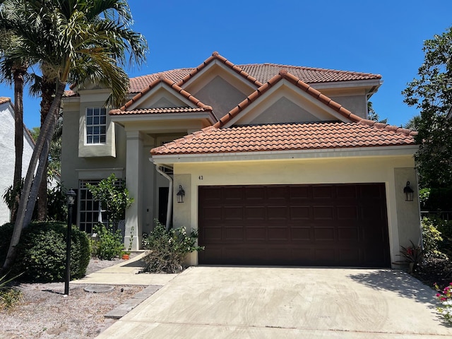 mediterranean / spanish home with a garage, driveway, stucco siding, and a tiled roof