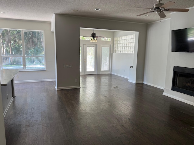 unfurnished living room featuring a ceiling fan, dark wood-style flooring, a textured ceiling, a fireplace, and baseboards
