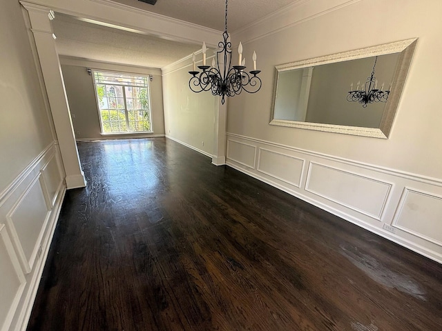 unfurnished dining area with a chandelier, a decorative wall, ornamental molding, dark wood-type flooring, and wainscoting