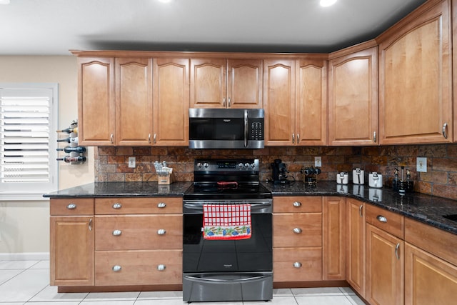 kitchen with black electric range oven, light tile patterned floors, stainless steel microwave, and dark stone counters