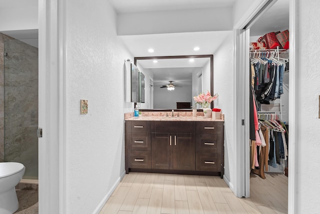 bathroom with baseboards, ceiling fan, a textured wall, vanity, and a walk in closet