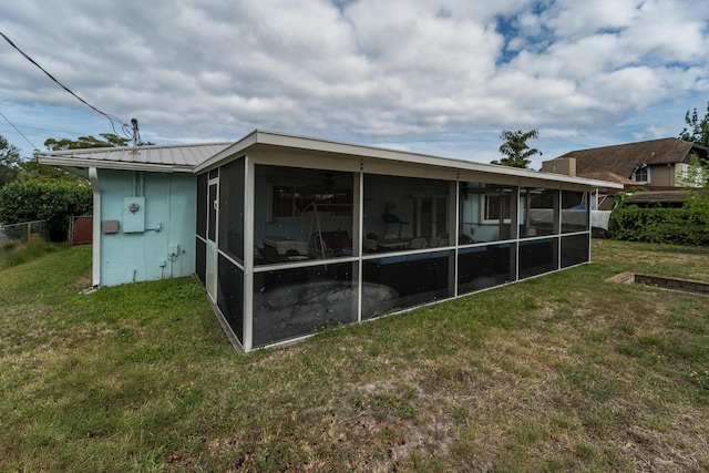 rear view of property featuring a sunroom, fence, a yard, and metal roof