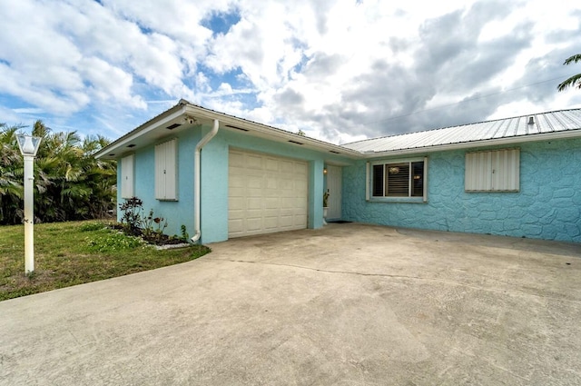 ranch-style house featuring metal roof, an attached garage, concrete driveway, and stucco siding