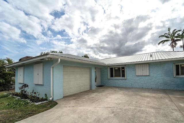 single story home featuring a garage, stucco siding, concrete driveway, and metal roof