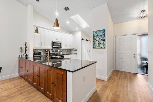 kitchen featuring visible vents, appliances with stainless steel finishes, light wood-type flooring, baseboards, and a peninsula