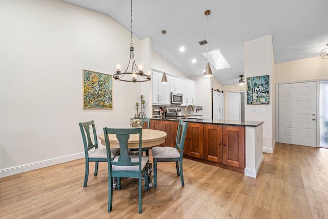 dining space featuring baseboards, lofted ceiling with skylight, light wood-style flooring, and visible vents