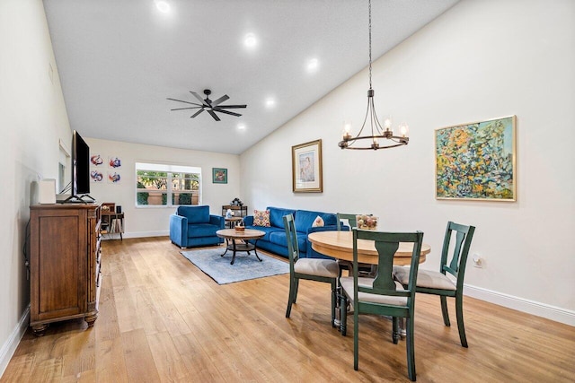 dining space featuring light wood-style floors, baseboards, ceiling fan with notable chandelier, and high vaulted ceiling