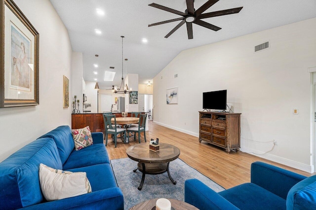living room featuring ceiling fan with notable chandelier, baseboards, lofted ceiling, light wood-type flooring, and visible vents