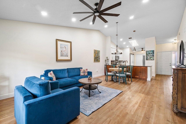 living area featuring vaulted ceiling with skylight, light wood-style floors, a ceiling fan, baseboards, and recessed lighting