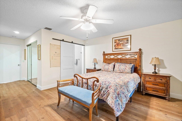 bedroom with a textured ceiling, a barn door, baseboards, and light wood-style floors