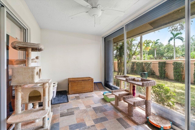 sunroom / solarium featuring stone finish flooring, ceiling fan, and a wealth of natural light