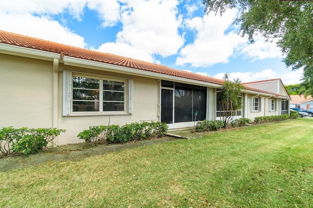 rear view of property featuring a lawn, stucco siding, and a tiled roof