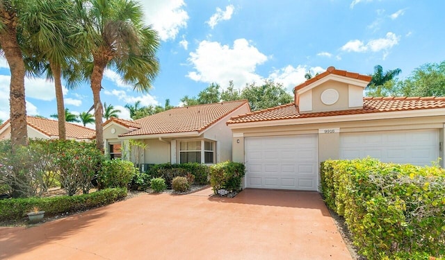 mediterranean / spanish-style house with a garage, stucco siding, a tiled roof, and concrete driveway
