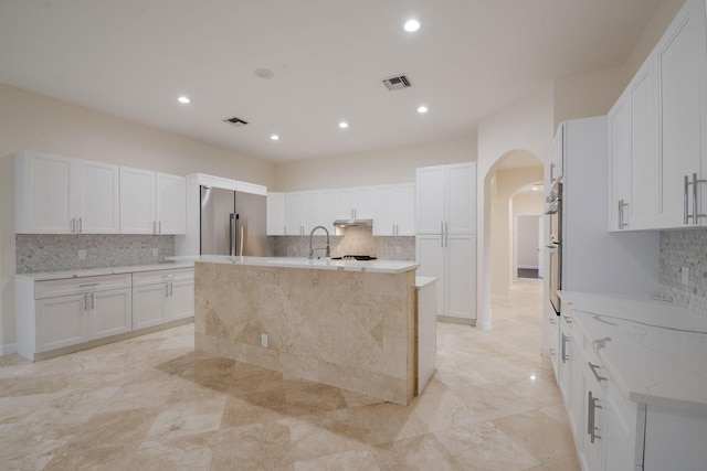8280 Woodsmuir Dr, Palm Beach Gardens, FL 33412 - kitchen with appliances with stainless steel finishes, arched walkways, decorative backsplash, a kitchen island with sink, and white cabinetry