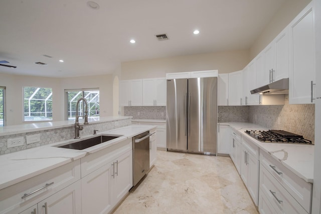 8280 Woodsmuir Dr, Palm Beach Gardens, FL 33412 - kitchen featuring appliances with stainless steel finishes, a sink, under cabinet range hood, backsplash, and light stone counters