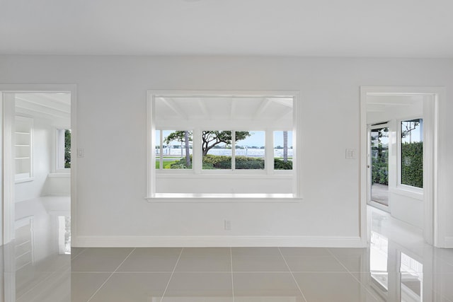 empty room with tile patterned floors, a wealth of natural light, and baseboards