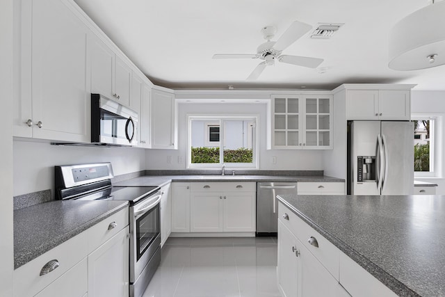 kitchen with glass insert cabinets, dark countertops, appliances with stainless steel finishes, and a healthy amount of sunlight