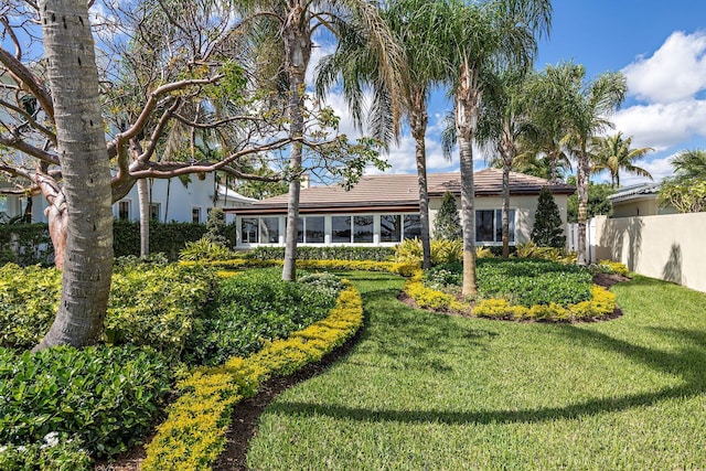 rear view of house with fence, a tiled roof, and a lawn