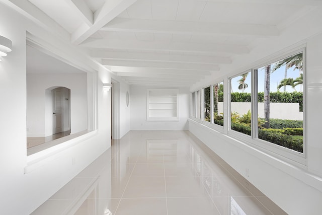 unfurnished sunroom with tile patterned flooring, arched walkways, and beam ceiling