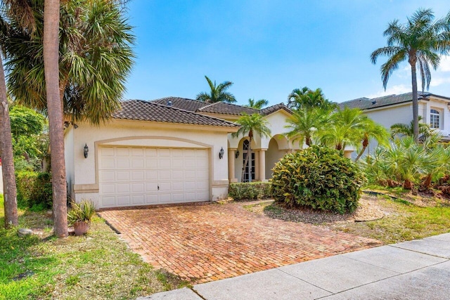 mediterranean / spanish-style home with an attached garage, a tile roof, decorative driveway, and stucco siding