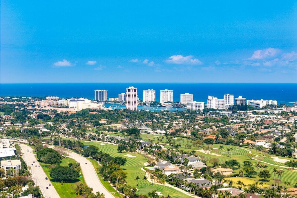 drone / aerial view with a water view, golf course view, and a view of city