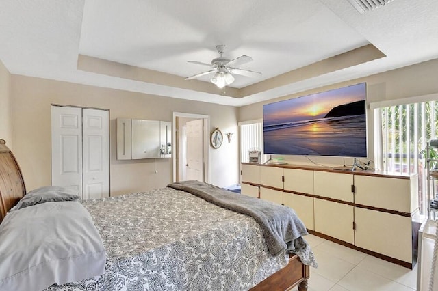 bedroom with a ceiling fan, a closet, light tile patterned flooring, a raised ceiling, and visible vents