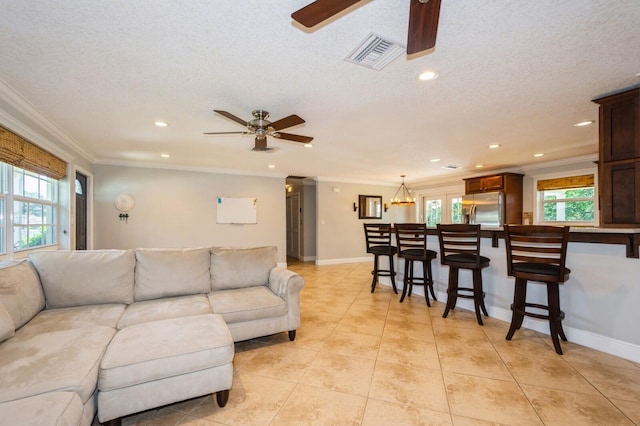 living room featuring a ceiling fan, visible vents, light tile patterned floors, and crown molding