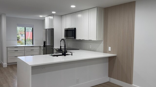 kitchen featuring light countertops, a sink, a peninsula, light wood-style flooring, and appliances with stainless steel finishes