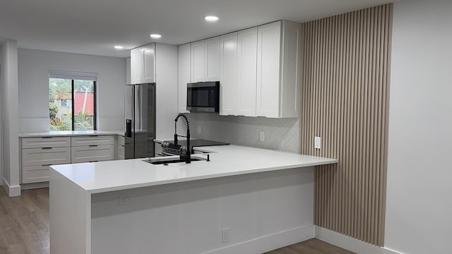 kitchen with a peninsula, light wood-style flooring, a sink, light countertops, and appliances with stainless steel finishes