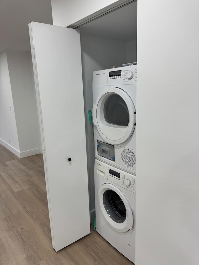 laundry area featuring stacked washer / drying machine, light wood-style flooring, baseboards, and laundry area
